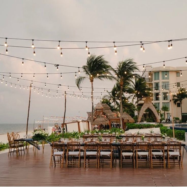 tables and chairs are set up on the beach for an outdoor wedding reception with string lights strung over them