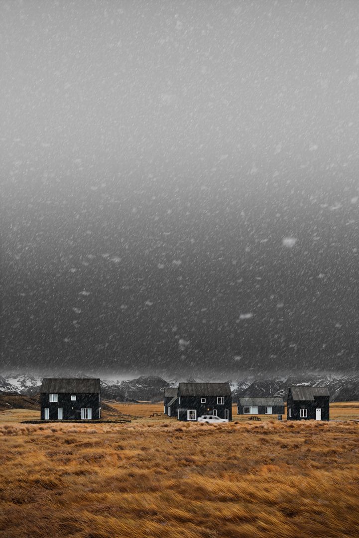 two black houses sitting on top of a dry grass field under a gray sky with snow flecks