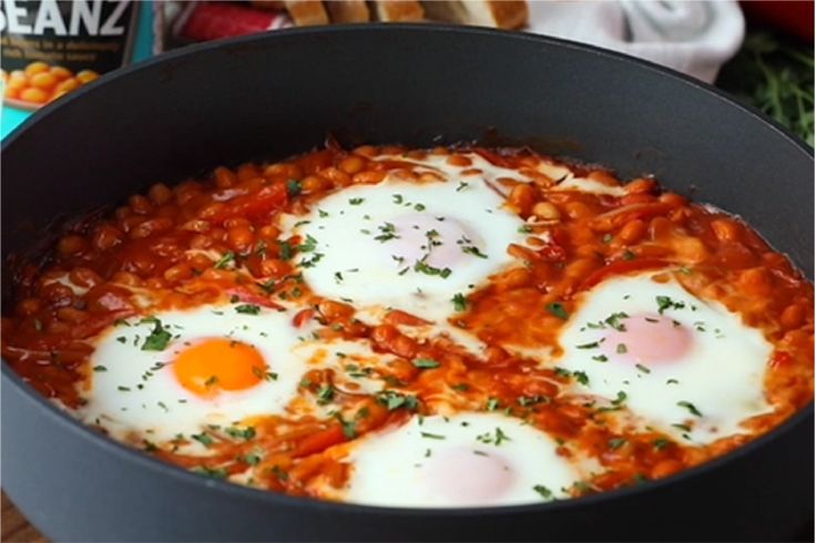 three fried eggs are in a skillet with tomato sauce