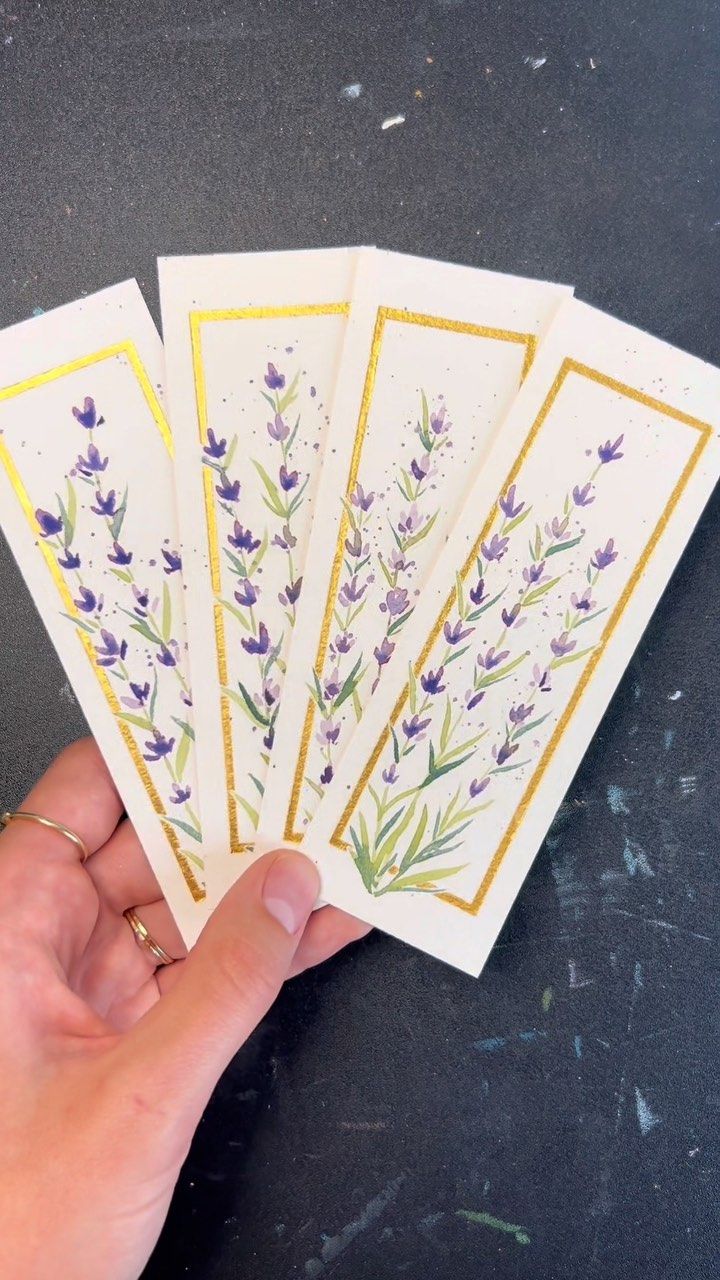 a hand holding five cards with purple flowers on them and gold trim around the edges