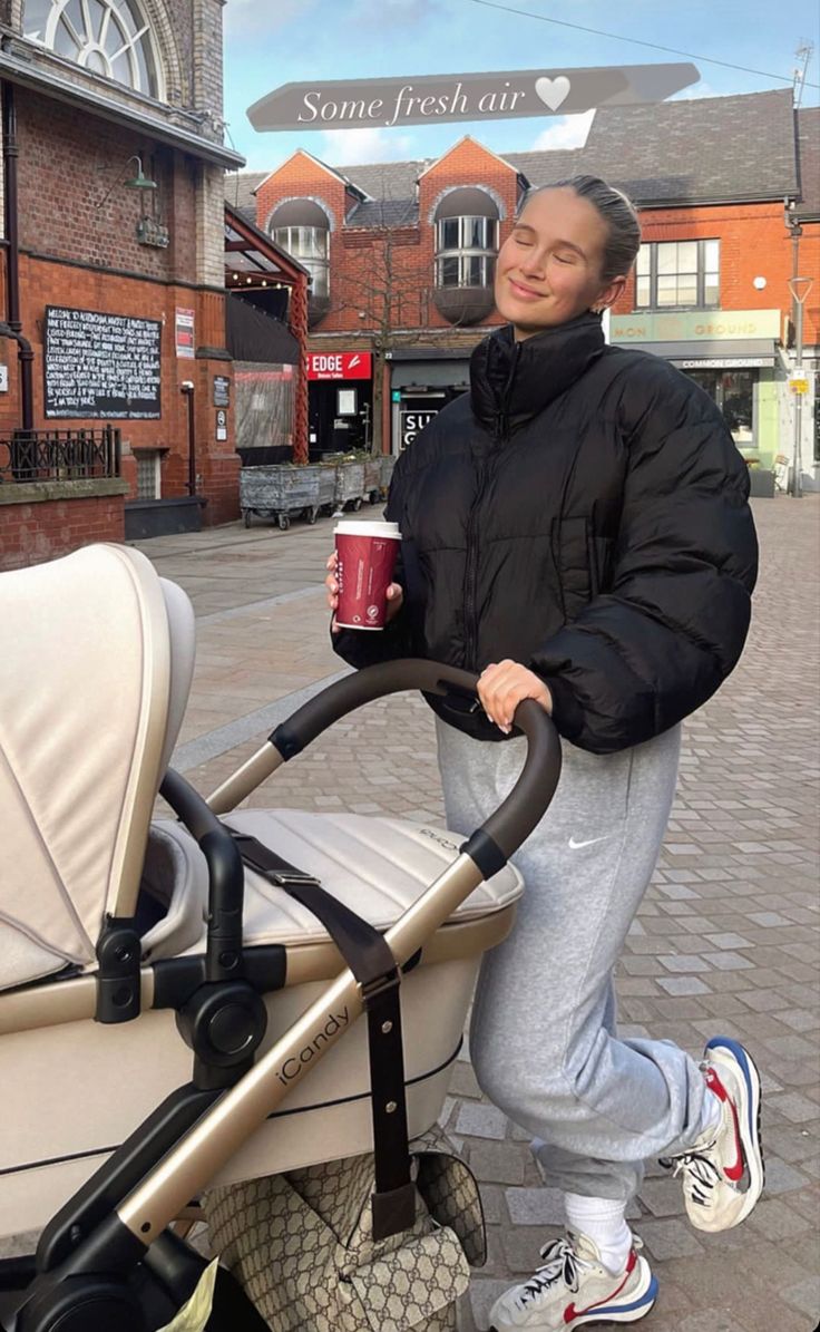 a man standing next to a baby stroller holding a coffee cup in his hand