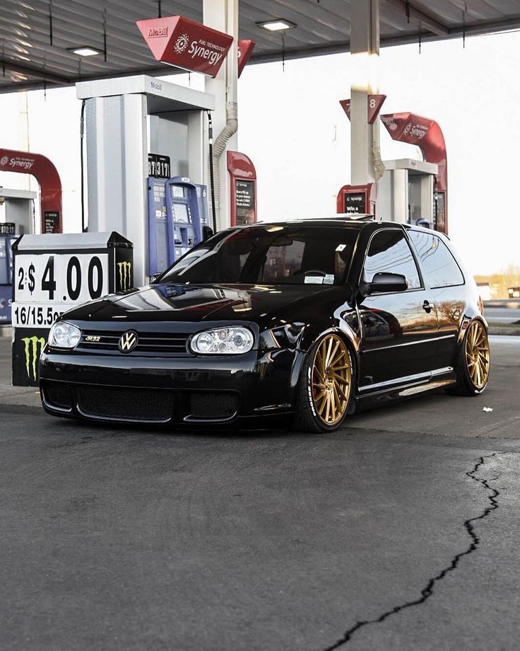 a black car with gold rims parked in front of a gas station fuel pump