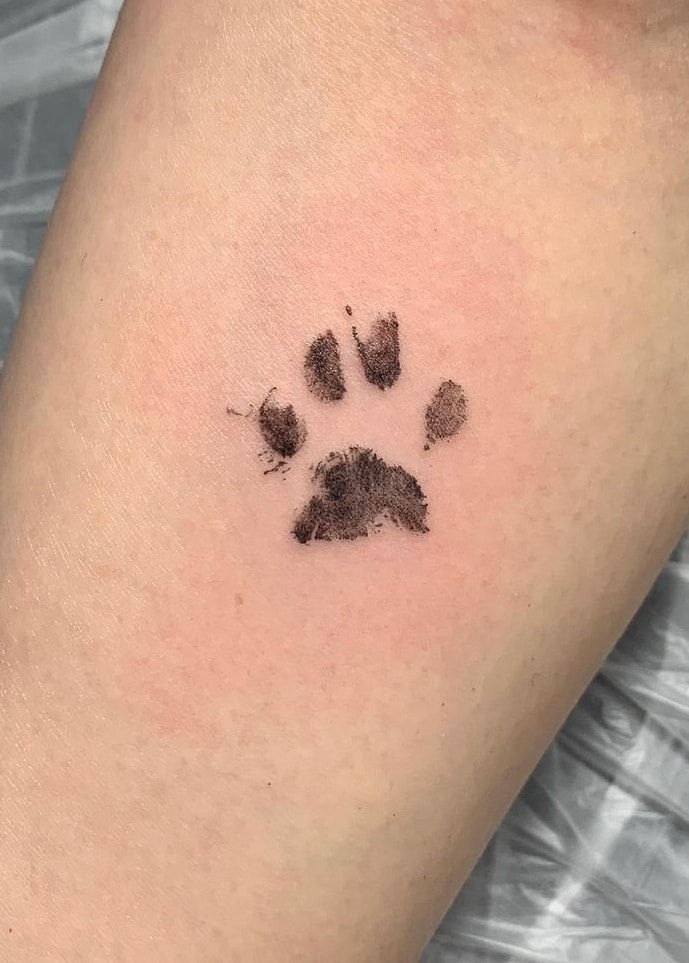 a small paw print on the back of a woman's leg, which is covered in black ink