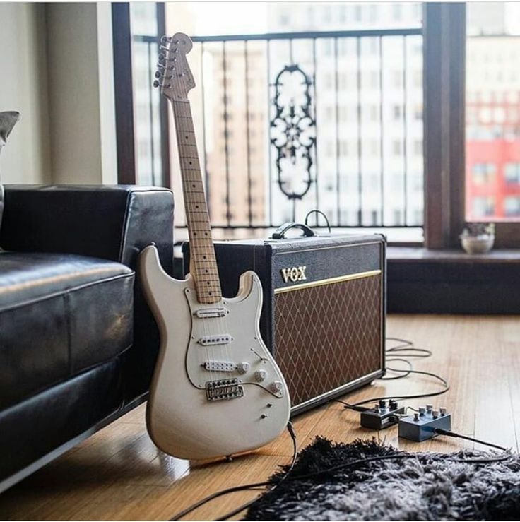 an electric guitar and amp sitting on the floor in front of a couch with a window