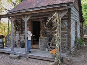 a man standing on the porch of a log cabin next to barrels and buckets