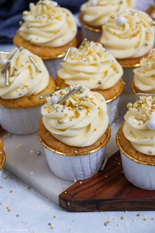 cupcakes with white frosting and gold sprinkles on a tray