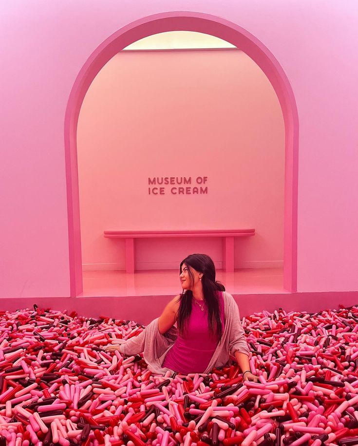 a woman sitting on the ground surrounded by crayons in front of a museum of ice cream