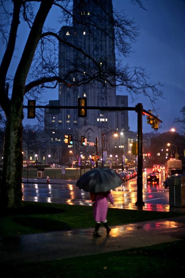 a woman with an umbrella is walking down the street at night in front of a tall building