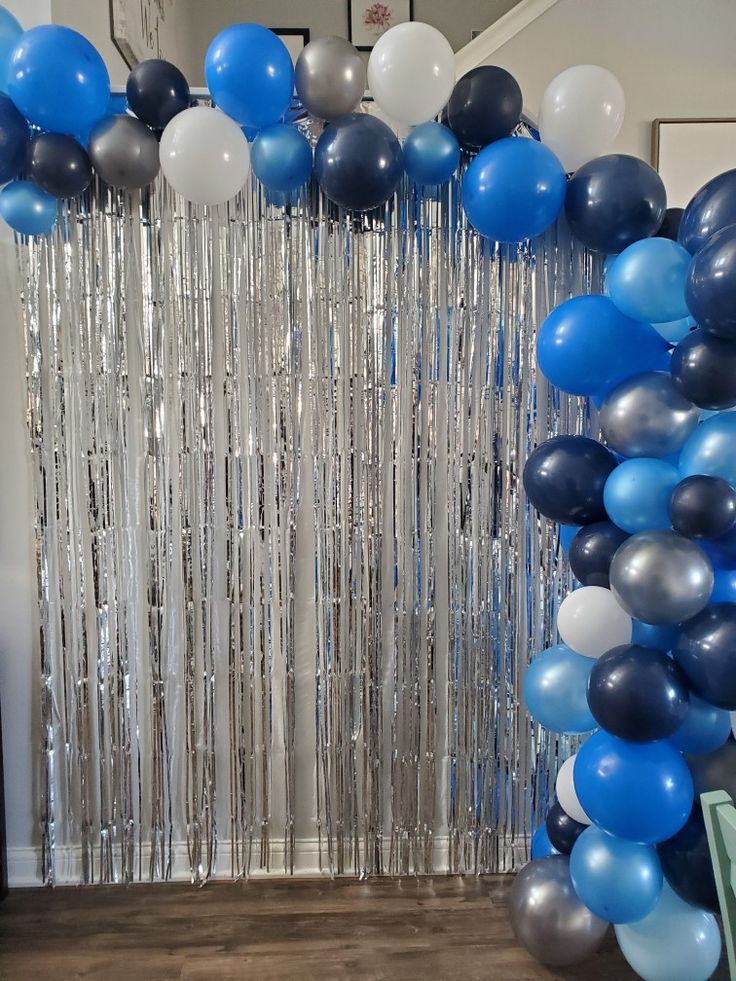 balloons and streamers are hanging from the ceiling in front of a curtain that is decorated with silver, blue and white confetti