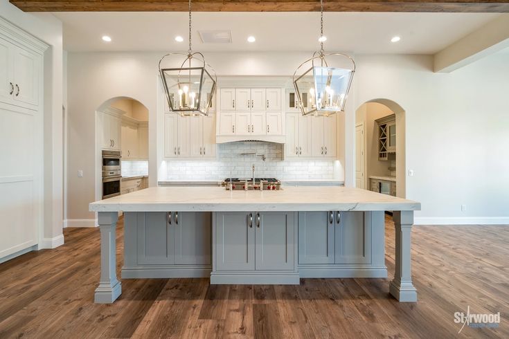 a large kitchen with an island in the middle and two pendant lights hanging from the ceiling