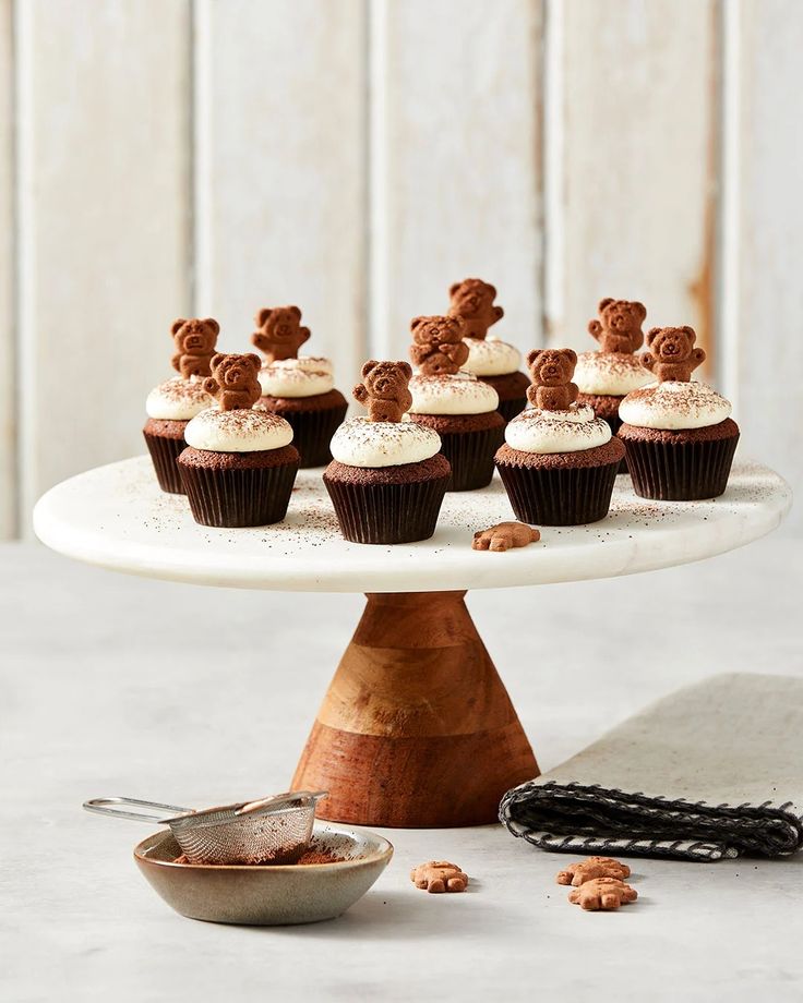 cupcakes with white frosting and chocolate teddy bears on top sitting on a cake plate