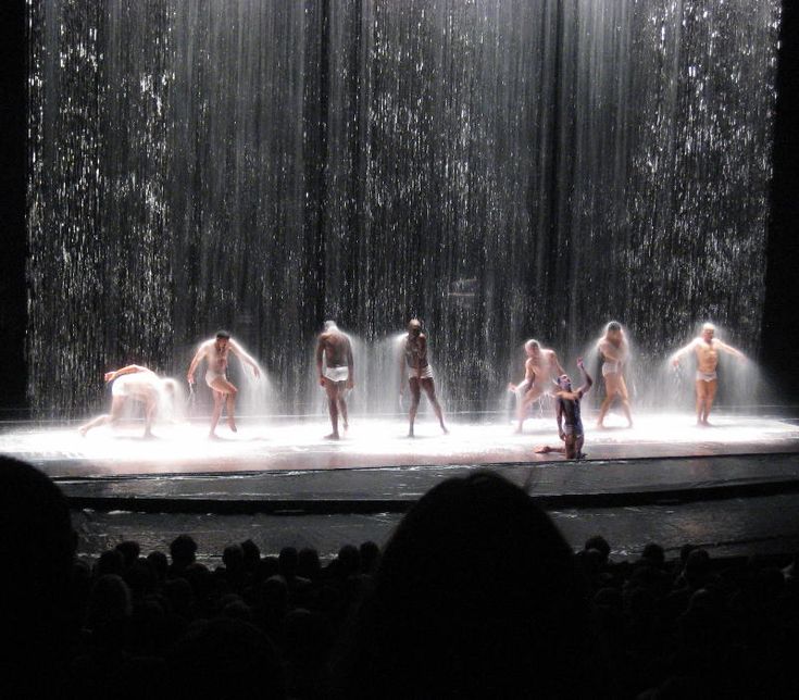 several naked people are standing on stage in front of a curtain with water coming from it