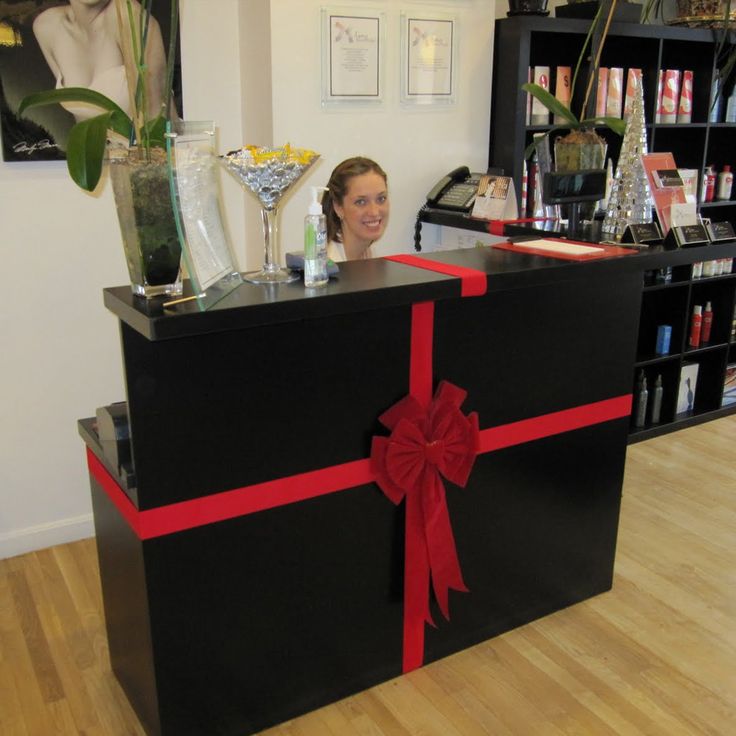 a woman is sitting behind a black box with a red ribbon on it in front of a bookshelf