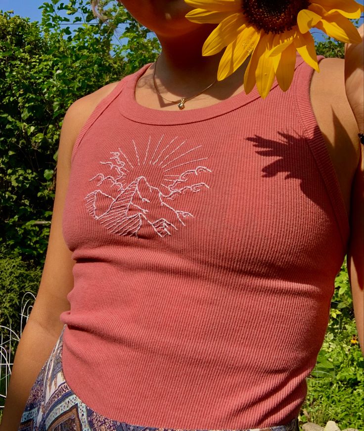 a woman with a sunflower on her head standing in front of some bushes and trees