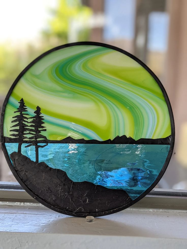 a glass plate sitting on top of a window sill next to a lake and trees