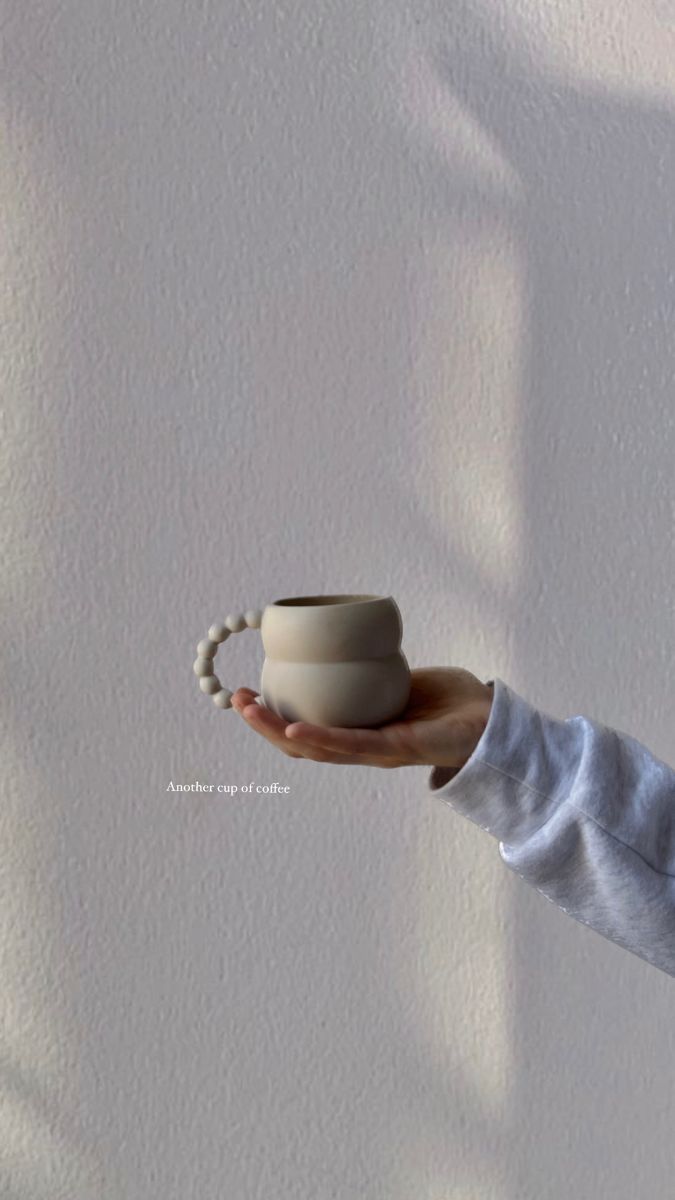 a person holding a cup in their hand with the shadow on the wall behind them