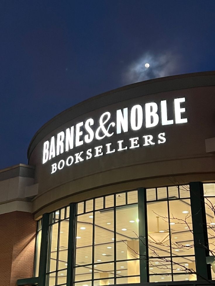 a store front at night with the moon in the sky above it and lights on