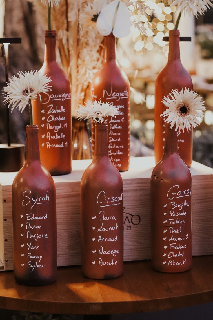 four wine bottles with names on them are sitting on a table next to some flowers