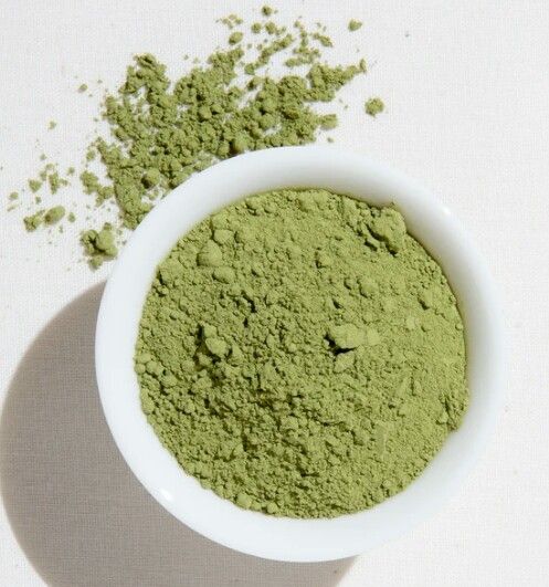 a white bowl filled with green powder on top of a table