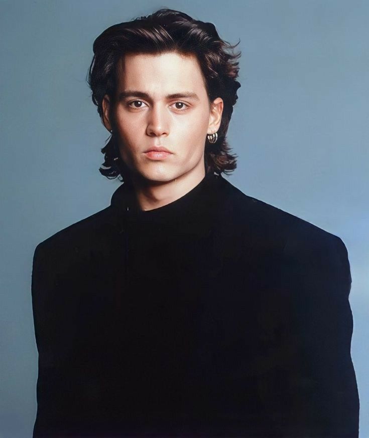 a man with long hair wearing a black shirt and earrings, posing for a portrait