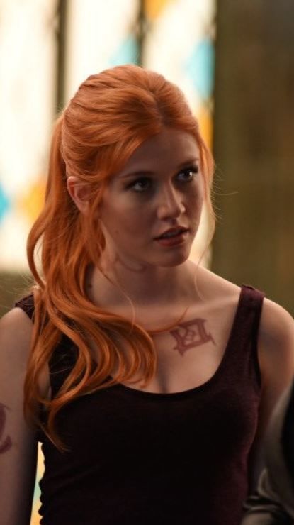 a woman with long red hair and tattoos on her chest is looking at the camera