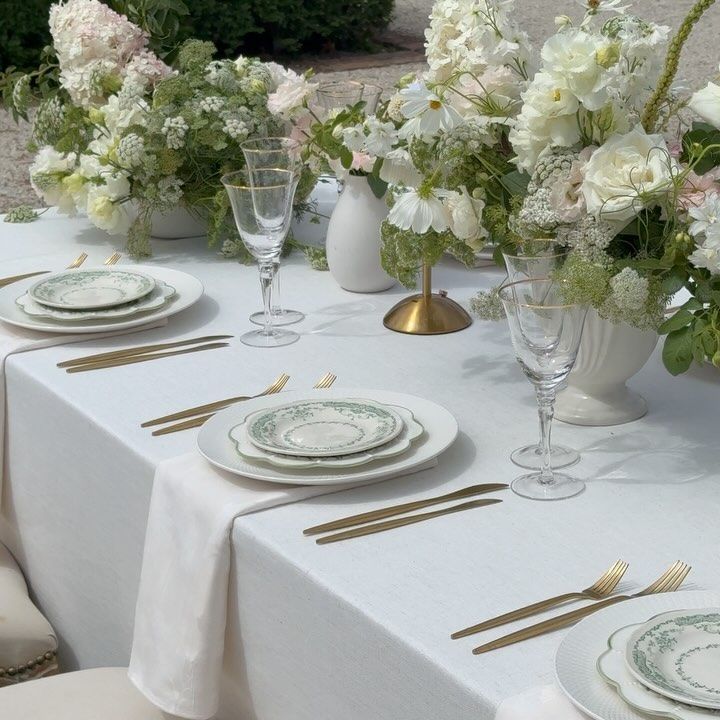 the table is set with white flowers and gold place settings