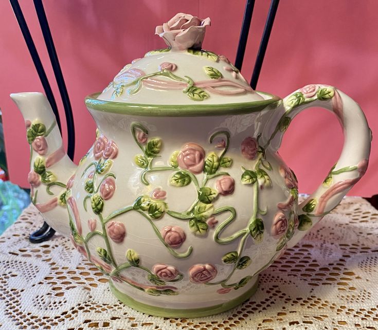 a ceramic teapot with flowers on it sitting on a doily covered tablecloth