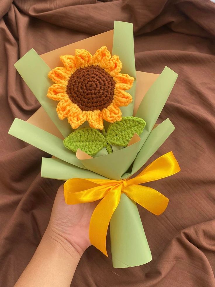 a hand holding a paper bouquet with a crocheted sunflower on it's center