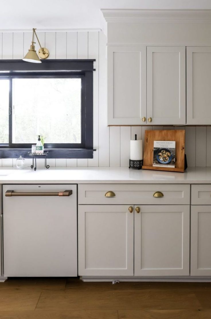 a kitchen with white cabinets and gold pulls on the drawers, an open dishwasher in front of a window