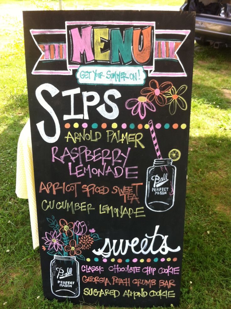 a menu sign is on the grass in front of a parked car and picnic table