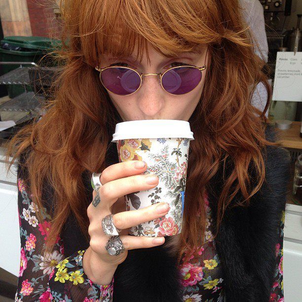 a woman with red hair and sunglasses drinking from a coffee cup