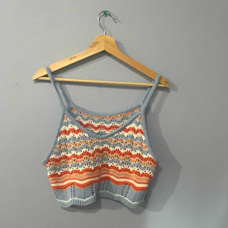 an orange, blue and white top hanging on a wooden hanger