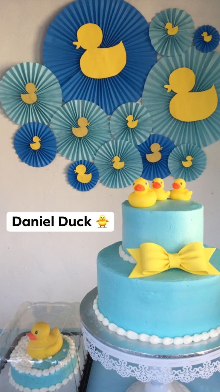 there is a blue cake with yellow rubber ducks on top and paper fans behind it