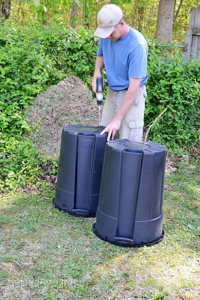 a man standing next to two black trash cans on top of a grass covered field