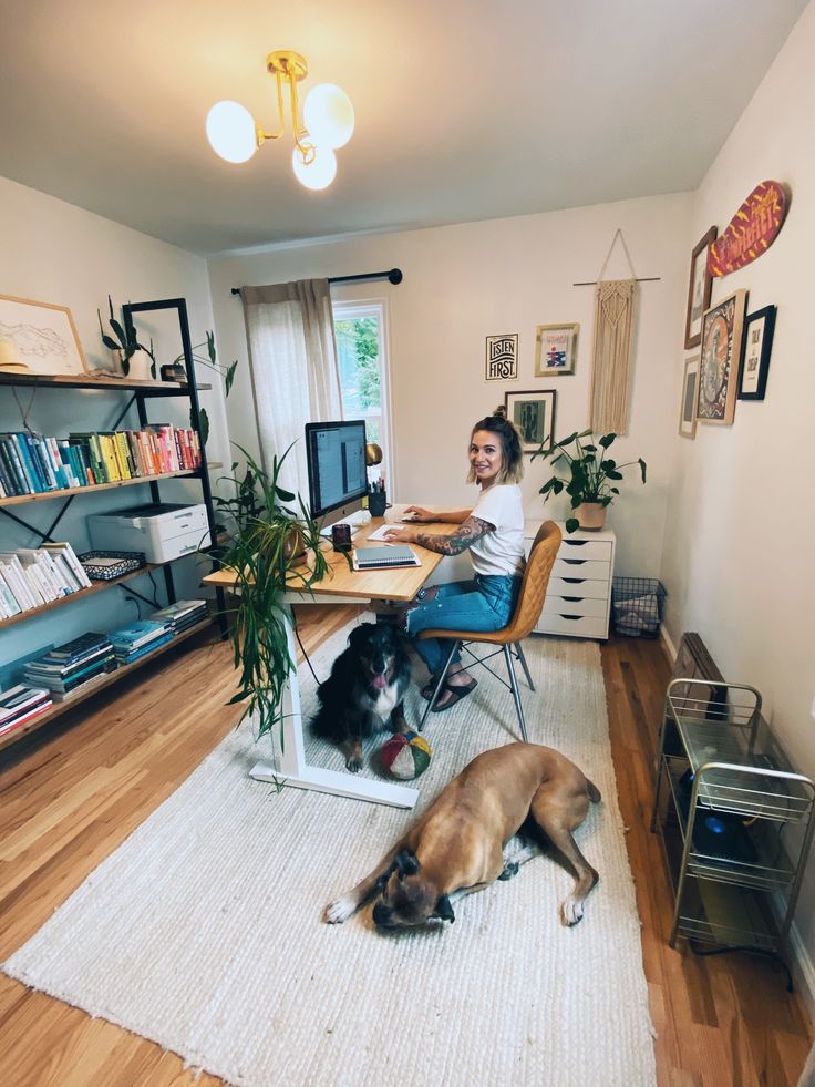 a man sitting at a computer desk with two dogs laying on the floor in front of him