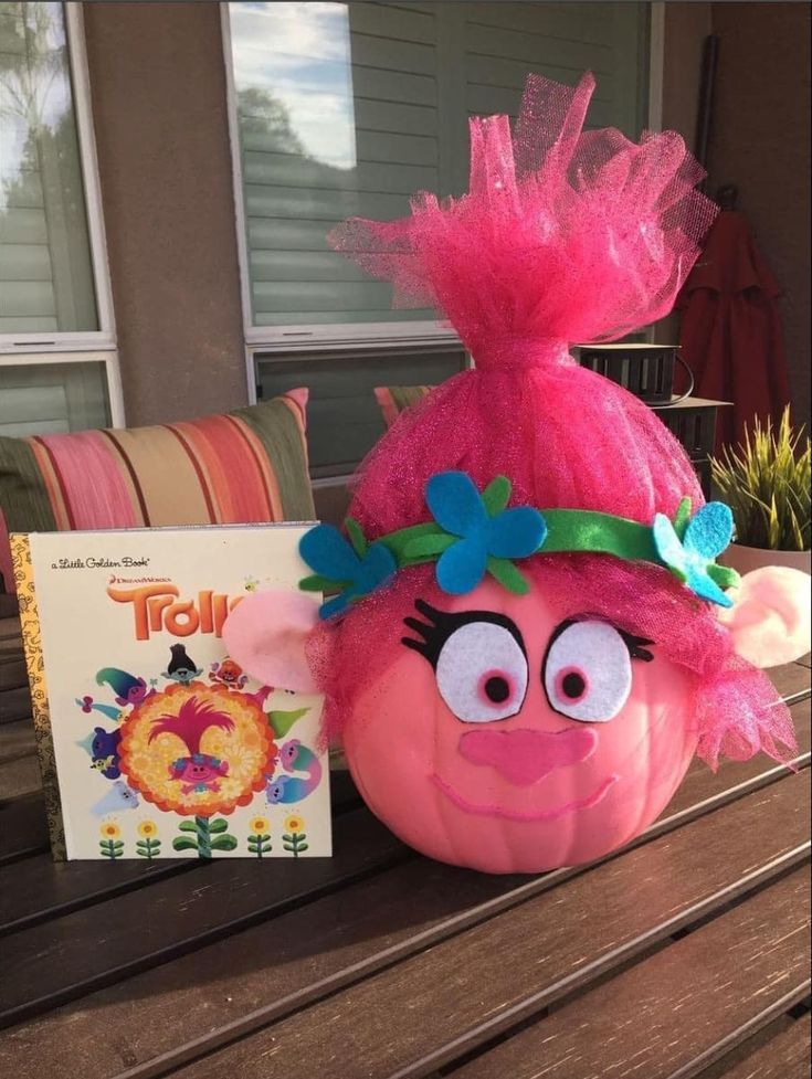 an orange pumpkin with a pink hat on it's head next to a book