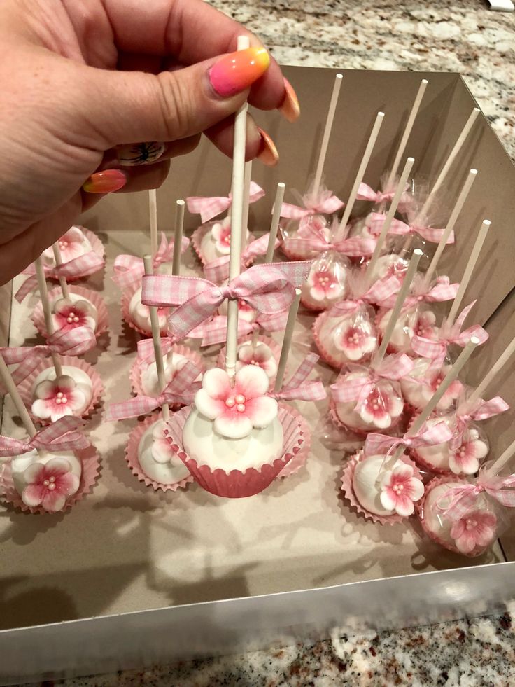 a person is holding up some cupcakes with white frosting and pink flowers on them