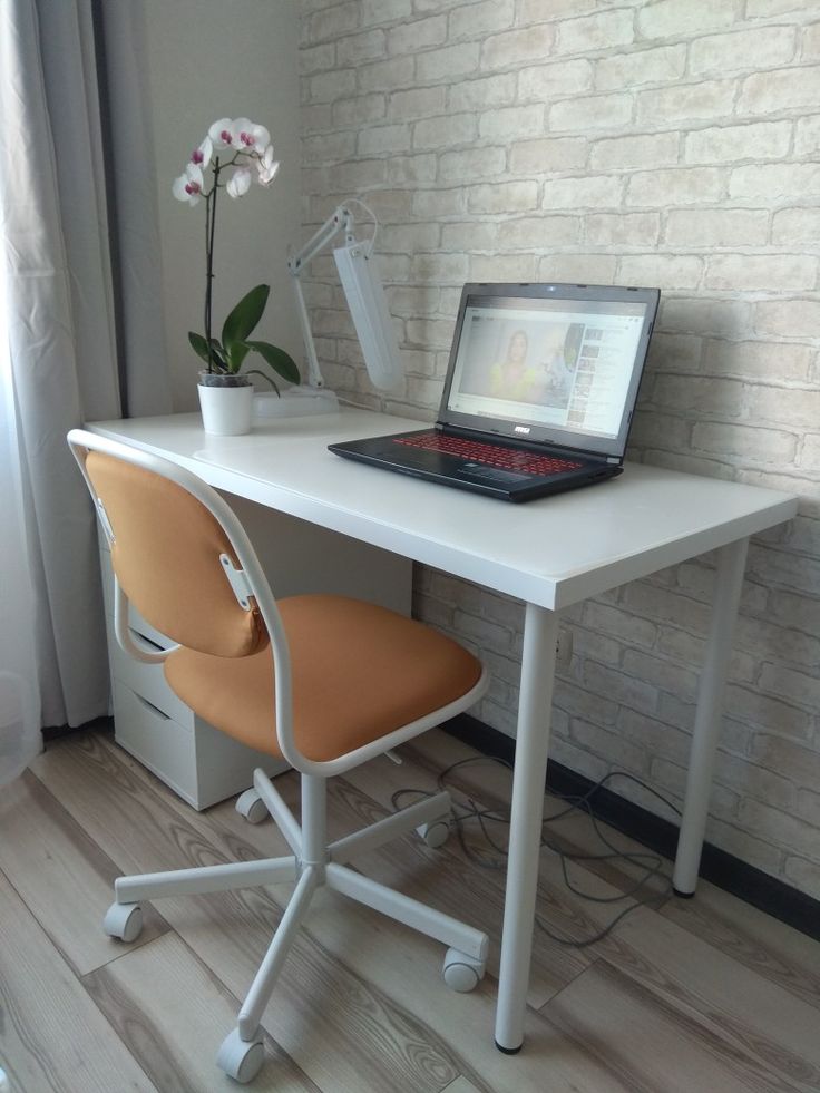 a laptop computer sitting on top of a white desk next to a flower in a vase