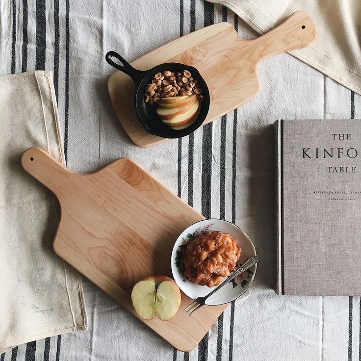 an apple and oatmeal bowl on a wooden cutting board next to a cookbook