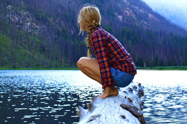 a woman sitting on top of a log next to a lake