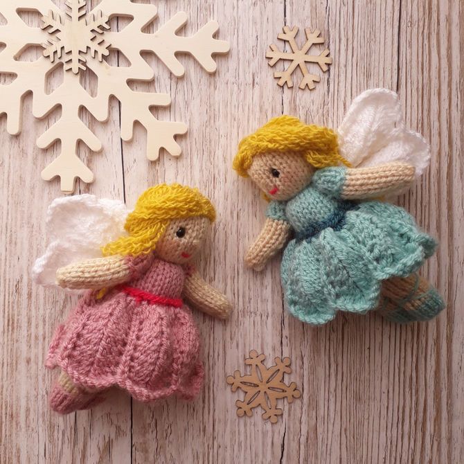 two crocheted angel ornaments sitting on top of a wooden table next to snowflakes