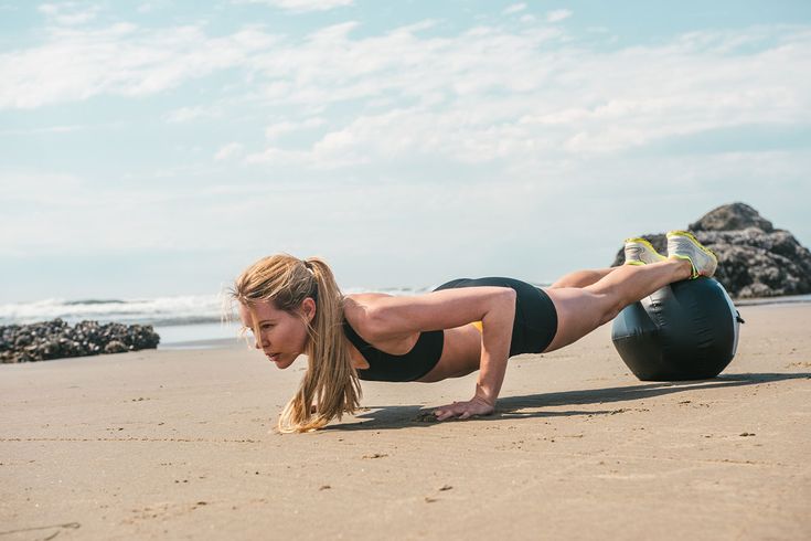 a woman is doing push ups on the beach with a ball in front of her