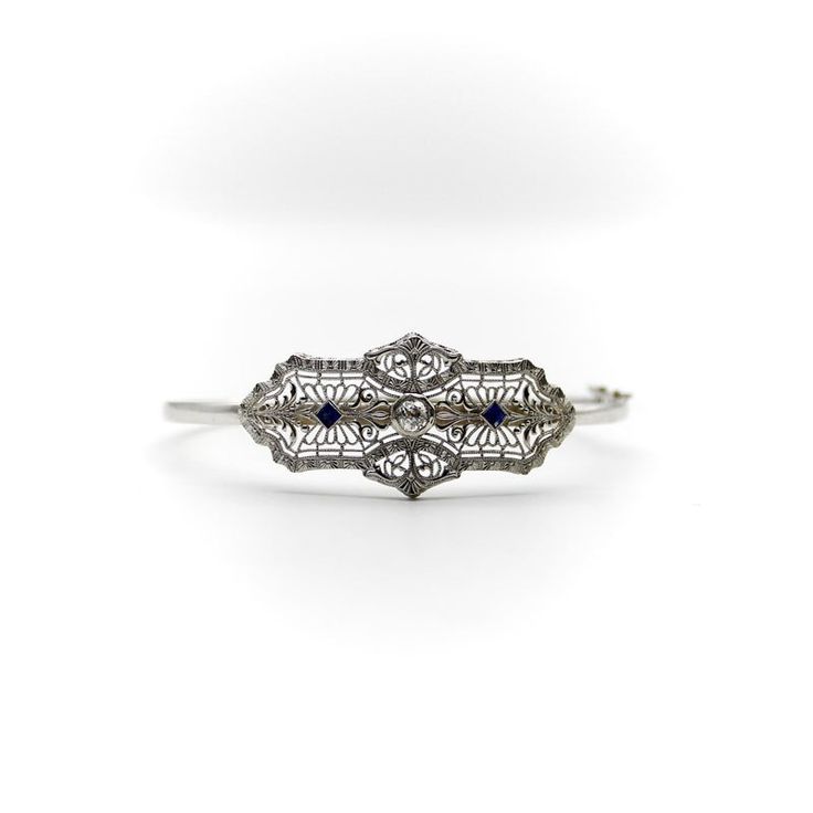 This is part of Chairish’s Fine Jewelry assortment.  A delicate Art Deco bracelet made of 14k white gold with a European cut diamond centre and two French cut sapphires on the side. The centrepiece has a symmetrical design, filled with delicate filagree and a scrolling foliate motif that is detailed and beautifully crafted. The diamond measures 4 mm and has .25 carat weight, it is G/H in colour and VS11 in clarity. The sapphires measure about 2.5 mm and have a well saturated blue tone. The centr Timeless White Gold Jewelry With Rose Cut Diamonds, Fine Jewelry With Sapphire And Single Cut Diamonds, Exquisite Diamond Cut Platinum Bracelet, Exquisite Platinum Diamond Cut Bracelet, Timeless 14k White Gold Jewelry With Single Cut Diamonds, Elegant Rose Cut Diamond Bracelets For Formal Occasions, Formal Sapphire Jewelry With Single Cut Diamonds, Exquisite Hand-set Diamond Platinum Bracelet, Exquisite Hand-set Platinum Diamond Bracelet