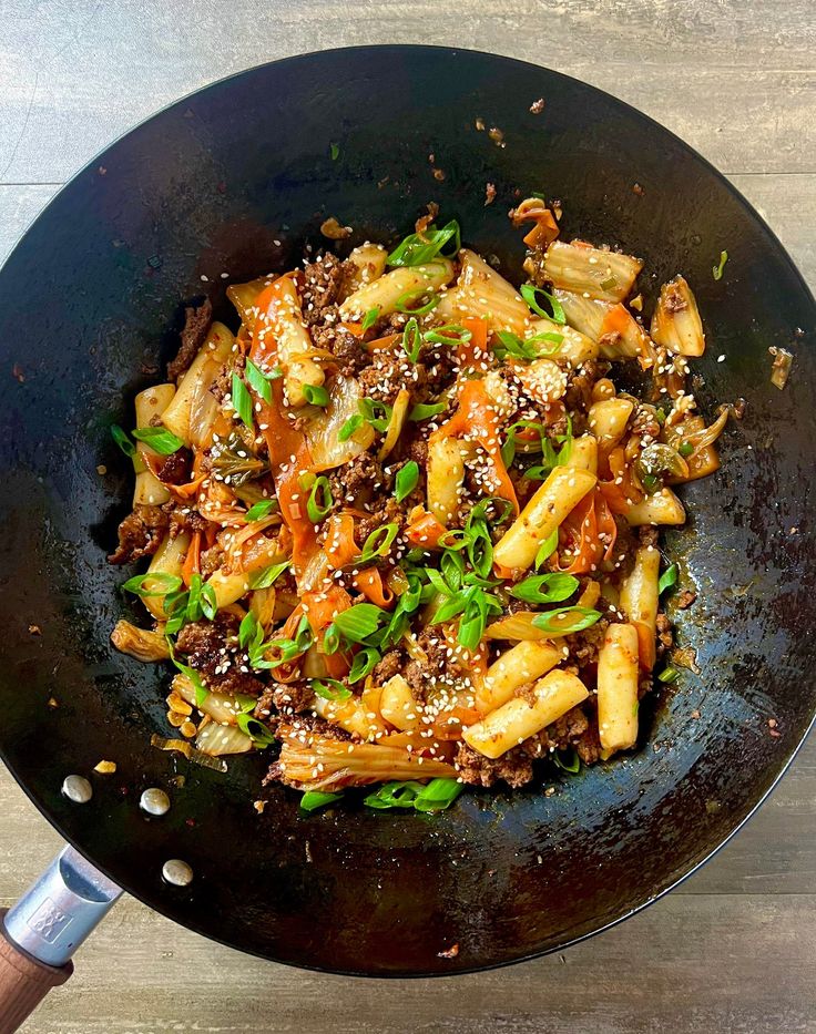 a wok filled with stir fry vegetables on top of a wooden table