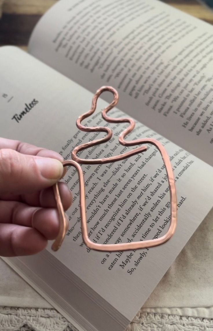 a person is holding an open book with a wire sculpture on it's cover