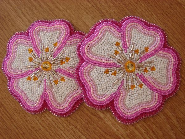 two pink and white flowers are sitting on a wooden table with beaded trimmings