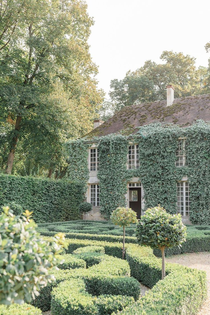 an old house covered in ivy surrounded by hedges