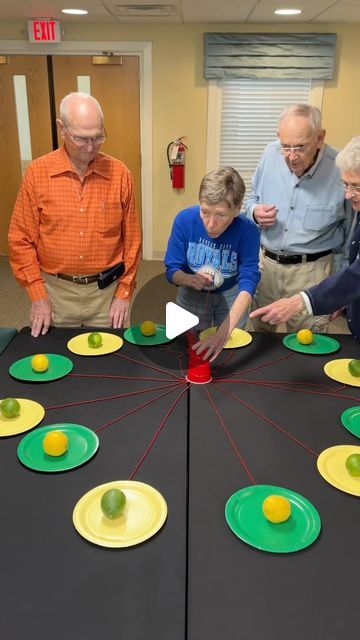 four people standing around a table with paper plates on it and two men looking at them