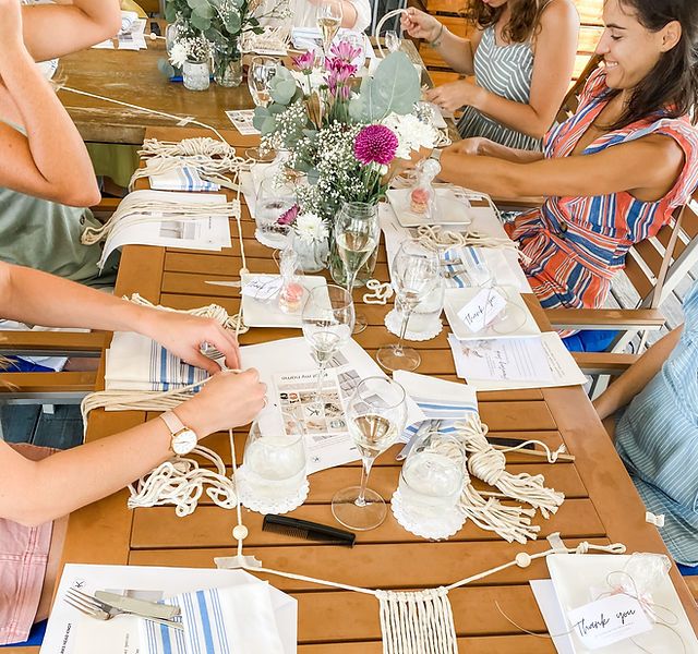 a group of people sitting around a wooden table with place settings on it and flowers in vases