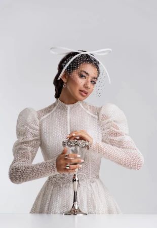 a woman wearing a white dress and veil holding a wine glass in front of her face